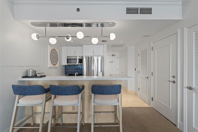 kitchen with appliances with stainless steel finishes, white cabinetry, a breakfast bar, decorative light fixtures, and light colored carpet