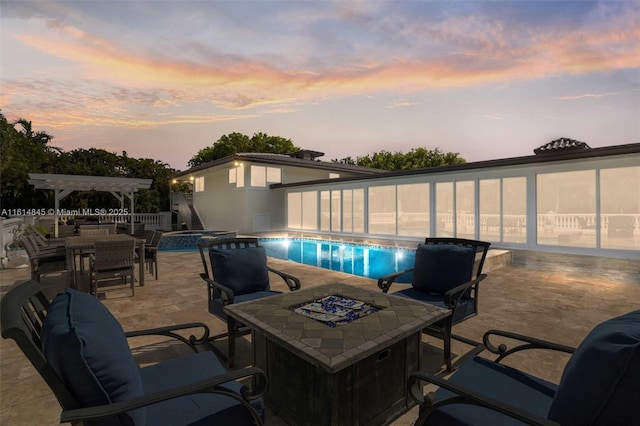 patio terrace at dusk featuring a pool with hot tub, a pergola, and a fire pit