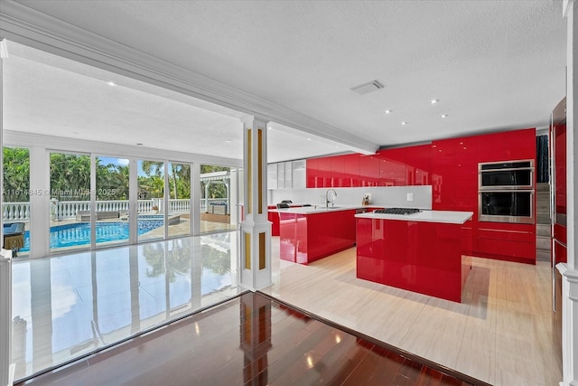 kitchen with stainless steel double oven, a center island, sink, decorative columns, and gas stovetop