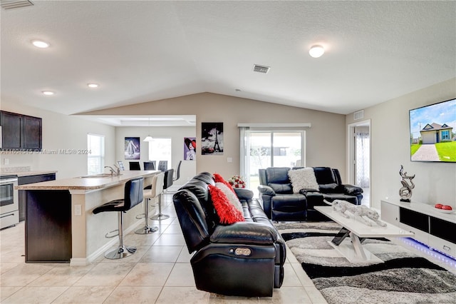 living room featuring a textured ceiling, sink, light tile patterned floors, and vaulted ceiling