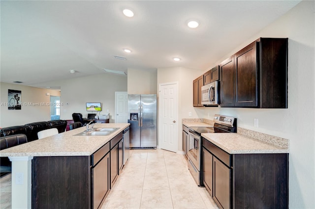 kitchen with dark brown cabinetry, sink, vaulted ceiling, a kitchen island with sink, and appliances with stainless steel finishes