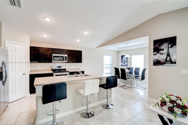 kitchen with a breakfast bar, dark brown cabinetry, stainless steel appliances, lofted ceiling, and an island with sink