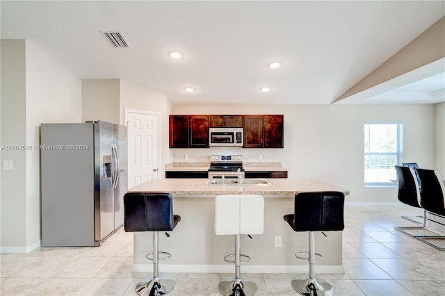 kitchen featuring sink, an island with sink, lofted ceiling, a breakfast bar area, and appliances with stainless steel finishes