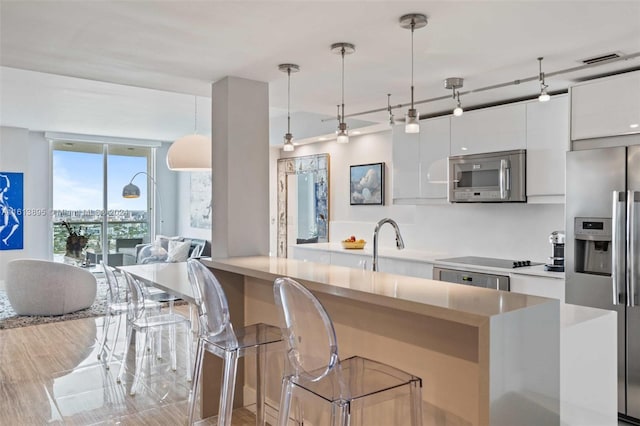 kitchen with appliances with stainless steel finishes, sink, decorative light fixtures, white cabinets, and a breakfast bar area