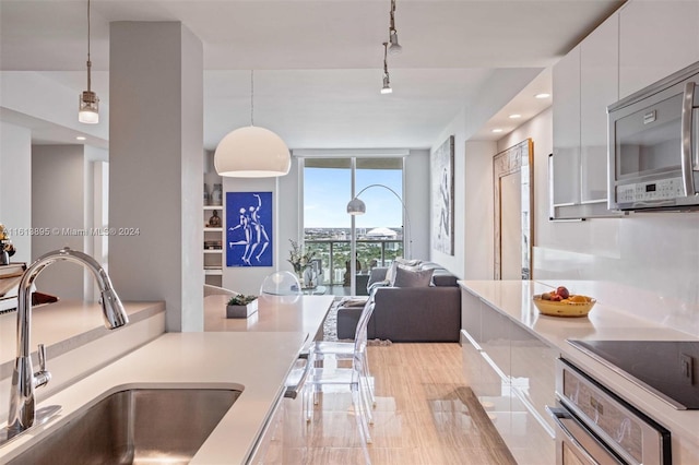 kitchen featuring pendant lighting, floor to ceiling windows, white cabinets, sink, and appliances with stainless steel finishes