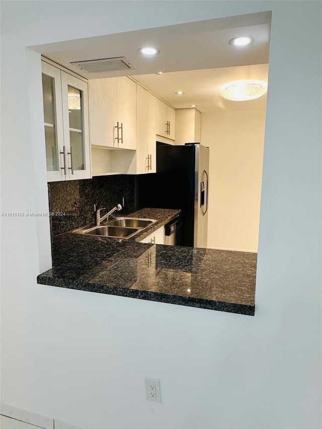 kitchen featuring white cabinetry, sink, kitchen peninsula, dark stone counters, and decorative backsplash