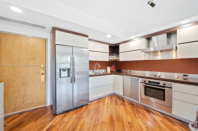 kitchen with wall chimney exhaust hood, stainless steel appliances, light hardwood / wood-style floors, and white cabinetry