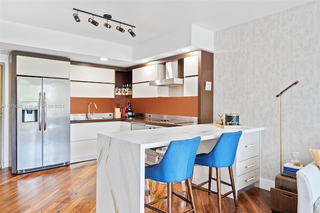 kitchen featuring rail lighting, white cabinetry, wall chimney exhaust hood, wood-type flooring, and appliances with stainless steel finishes