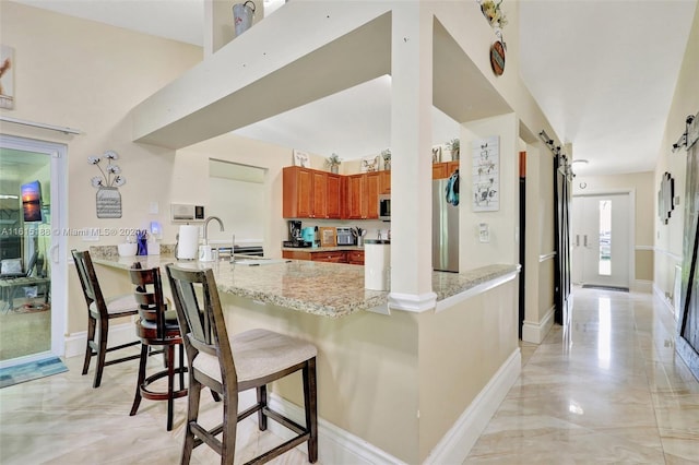 kitchen with a breakfast bar, kitchen peninsula, a barn door, appliances with stainless steel finishes, and light stone countertops