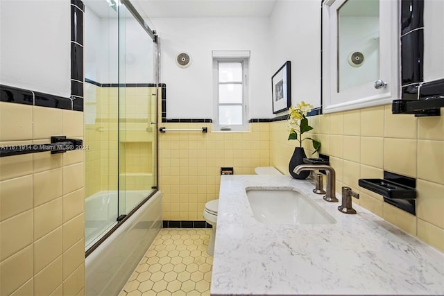 full bathroom featuring tile patterned flooring, bath / shower combo with glass door, toilet, vanity, and tile walls