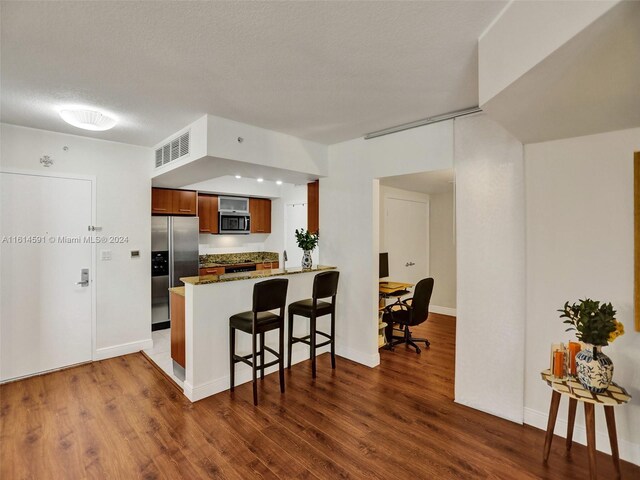 kitchen featuring appliances with stainless steel finishes, dark wood-type flooring, kitchen peninsula, and a kitchen bar