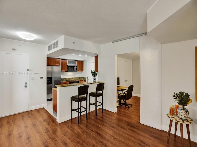 kitchen with a breakfast bar, appliances with stainless steel finishes, dark hardwood / wood-style floors, a textured ceiling, and kitchen peninsula