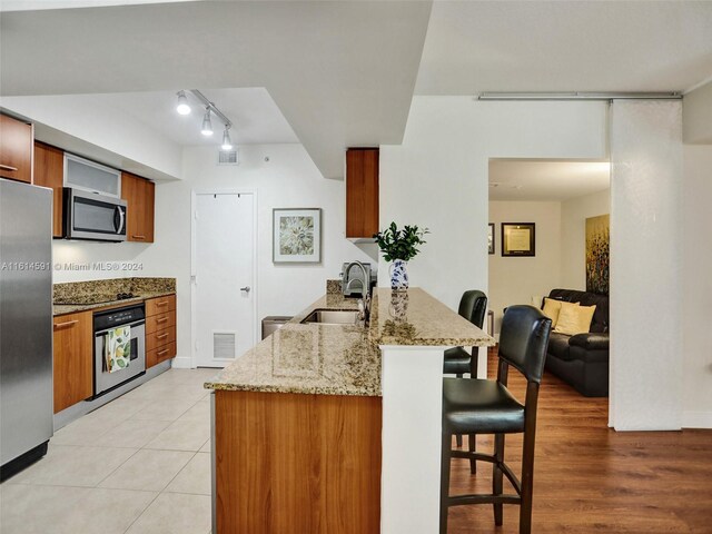 kitchen featuring light stone countertops, stainless steel appliances, rail lighting, a breakfast bar, and sink