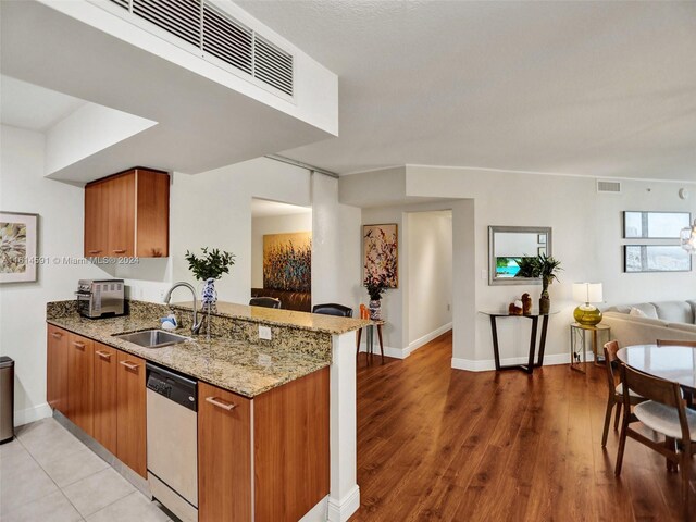 kitchen featuring light stone countertops, light hardwood / wood-style flooring, kitchen peninsula, white dishwasher, and sink