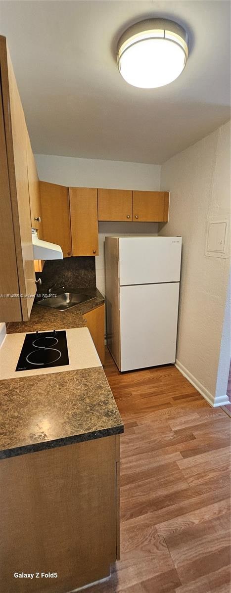 kitchen featuring stovetop, sink, white fridge, and light wood-type flooring