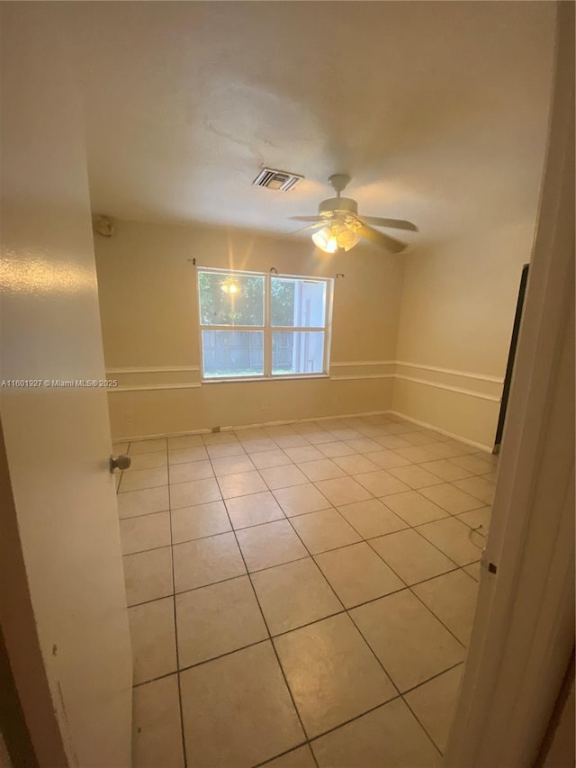 empty room with light tile patterned flooring, baseboards, ceiling fan, and visible vents