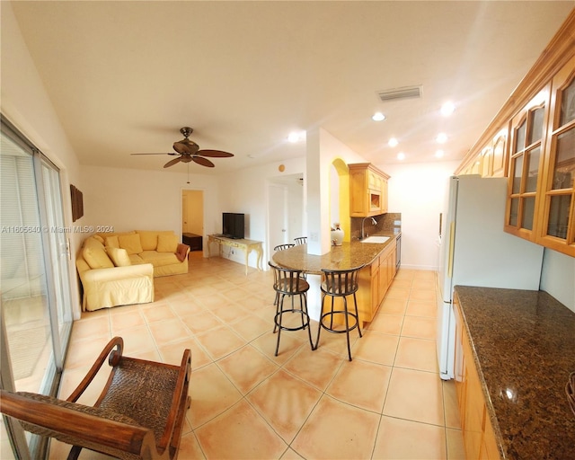 kitchen featuring sink, ceiling fan, light tile floors, and a kitchen bar