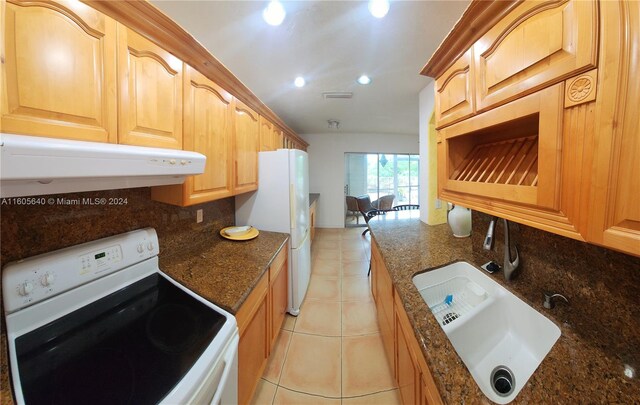 kitchen with stove, tasteful backsplash, dark stone countertops, sink, and light tile floors