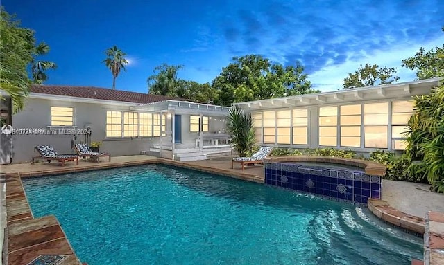 pool at dusk featuring a patio area and an in ground hot tub