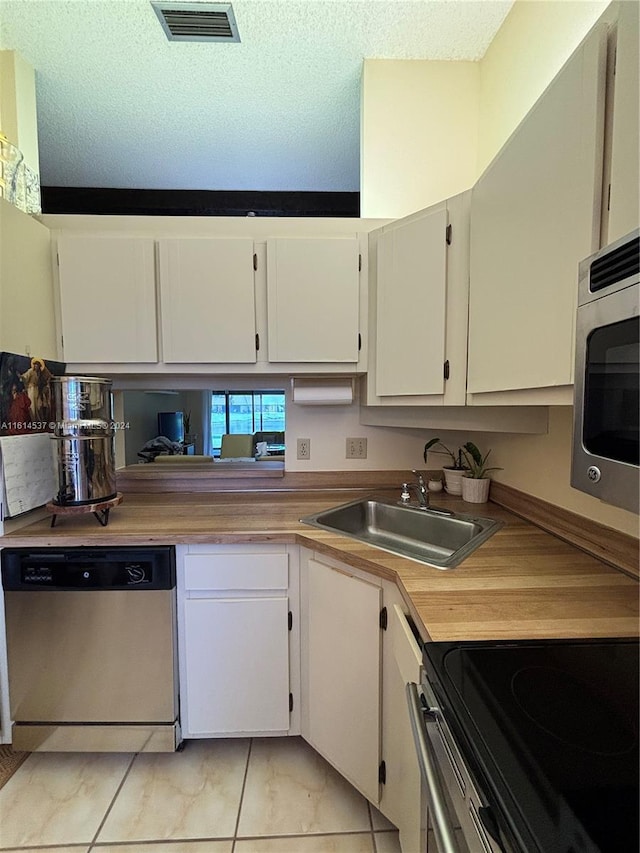 kitchen with white cabinetry, stainless steel appliances, light tile patterned flooring, a textured ceiling, and sink