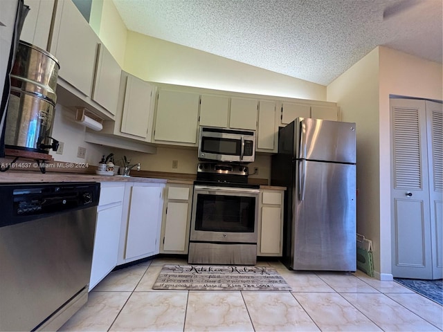 kitchen featuring vaulted ceiling, white cabinetry, appliances with stainless steel finishes, a textured ceiling, and light tile patterned floors