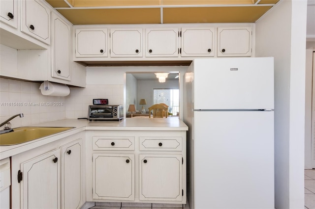 kitchen with white refrigerator, white cabinets, backsplash, sink, and light tile flooring