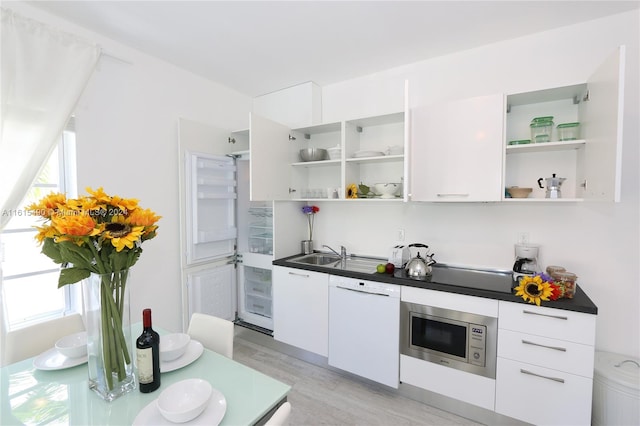 kitchen with white dishwasher, white cabinetry, light hardwood / wood-style floors, stainless steel microwave, and sink