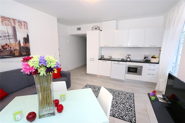 kitchen featuring light hardwood / wood-style flooring, dishwasher, stainless steel microwave, white cabinetry, and sink