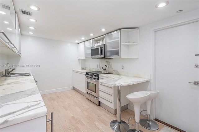 kitchen featuring sink, light hardwood / wood-style flooring, light stone counters, stainless steel appliances, and white cabinets