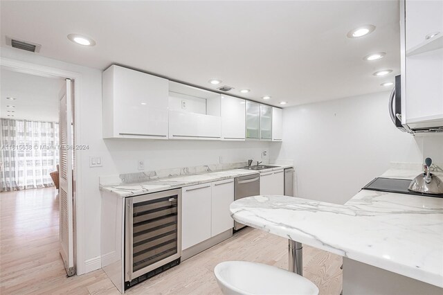 kitchen with white cabinets, light hardwood / wood-style flooring, light stone counters, and wine cooler