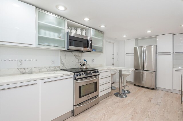 kitchen featuring backsplash, appliances with stainless steel finishes, light hardwood / wood-style flooring, light stone counters, and white cabinetry