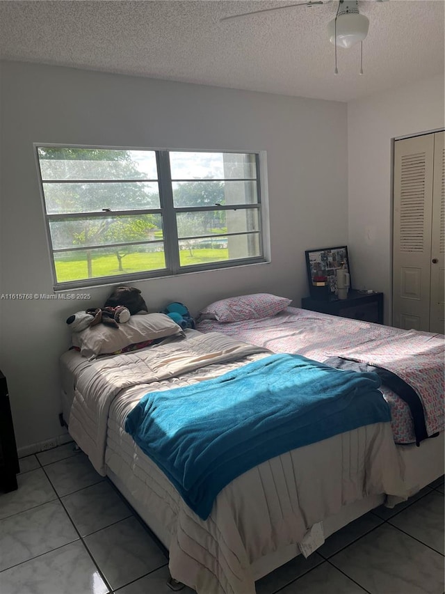 tiled bedroom with a textured ceiling, ceiling fan, and a closet