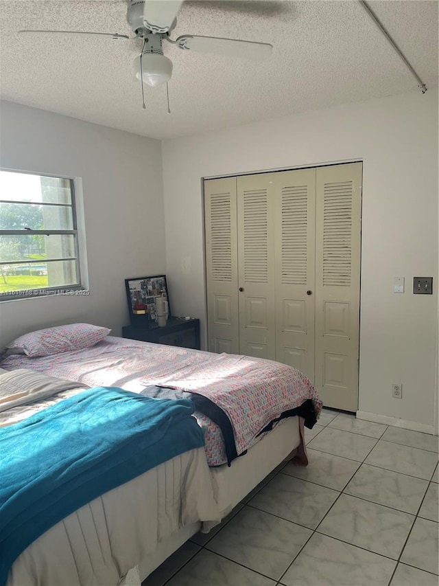 tiled bedroom with ceiling fan, a closet, and a textured ceiling