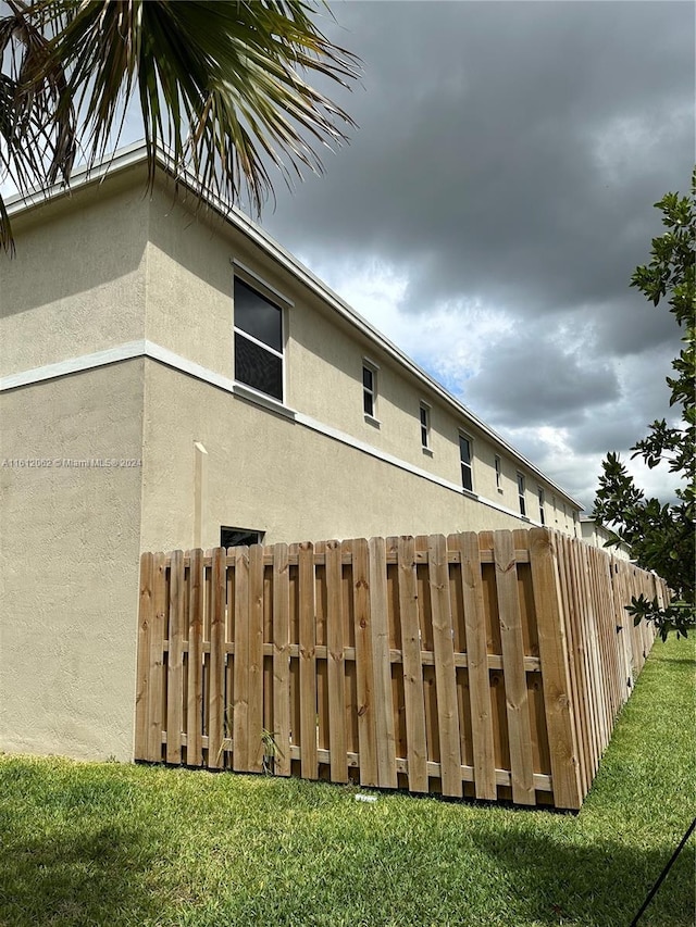 view of property exterior featuring stucco siding, a lawn, and fence