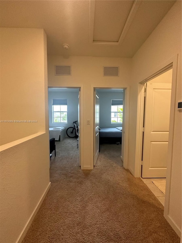 hall featuring a tray ceiling, visible vents, baseboards, and light colored carpet