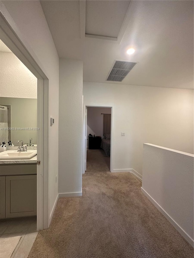 hallway featuring baseboards, light colored carpet, visible vents, and a sink