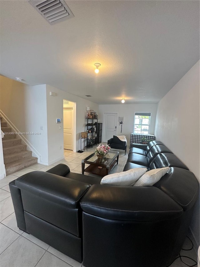 living room with light tile patterned flooring, visible vents, a textured ceiling, and stairs