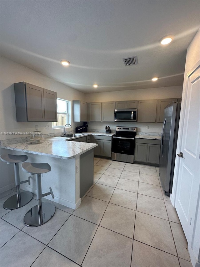 kitchen with visible vents, gray cabinetry, a peninsula, stainless steel appliances, and a sink