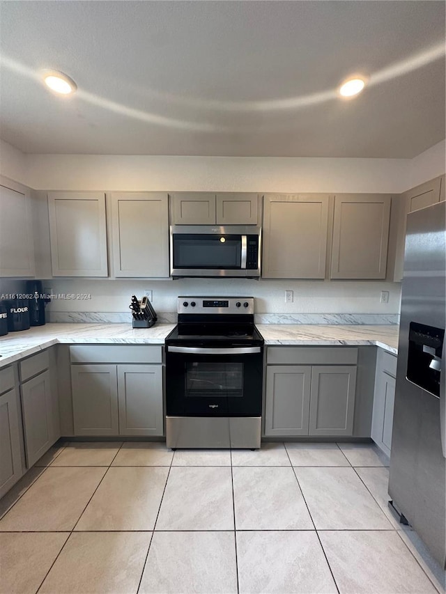 kitchen with light tile patterned flooring, gray cabinetry, stainless steel appliances, and light stone countertops