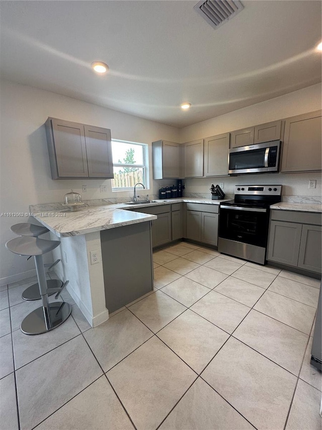 kitchen featuring visible vents, a kitchen bar, gray cabinetry, appliances with stainless steel finishes, and a peninsula