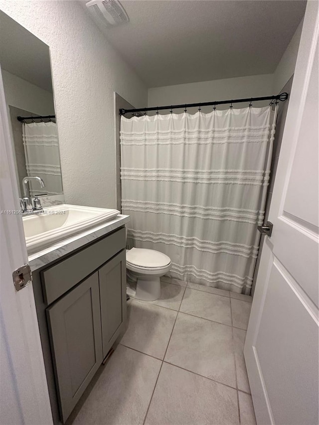 bathroom with vanity, visible vents, tile patterned flooring, toilet, and a textured wall