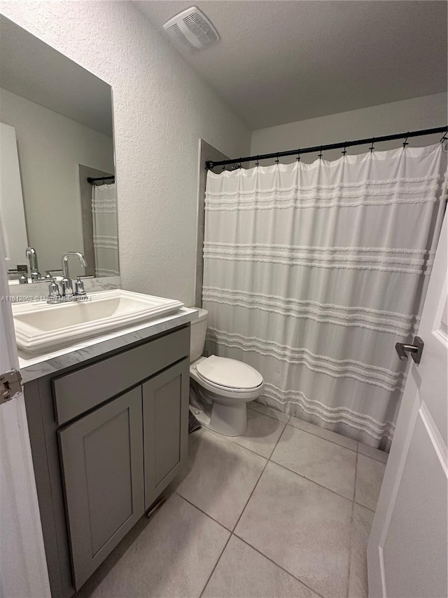 bathroom featuring tile patterned flooring, visible vents, toilet, a textured wall, and vanity