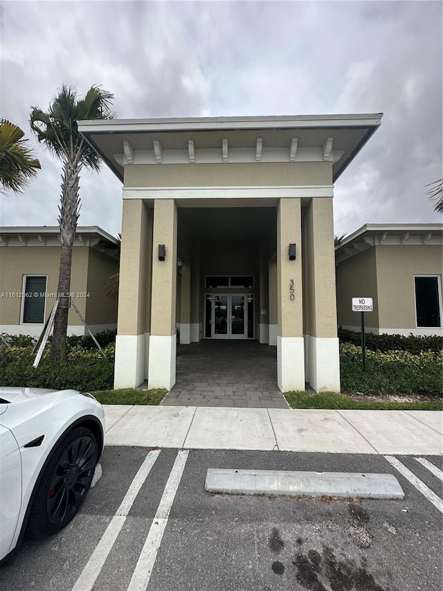 entrance to property featuring stucco siding, french doors, and uncovered parking