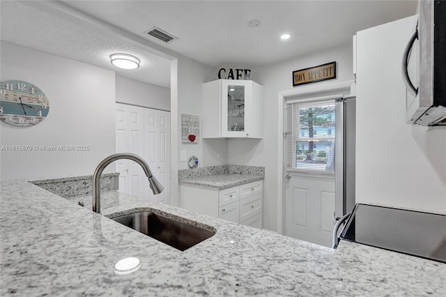 kitchen featuring white cabinets, a textured ceiling, light stone countertops, and sink