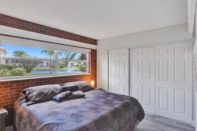 bedroom featuring brick wall, a textured ceiling, a closet, and light hardwood / wood-style floors