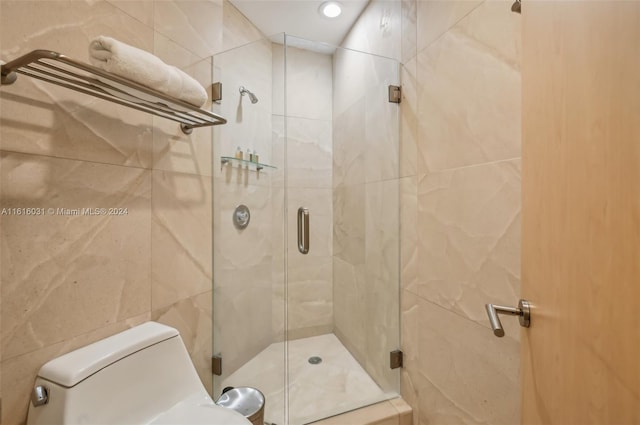 bathroom featuring toilet, tile walls, and a shower with shower door