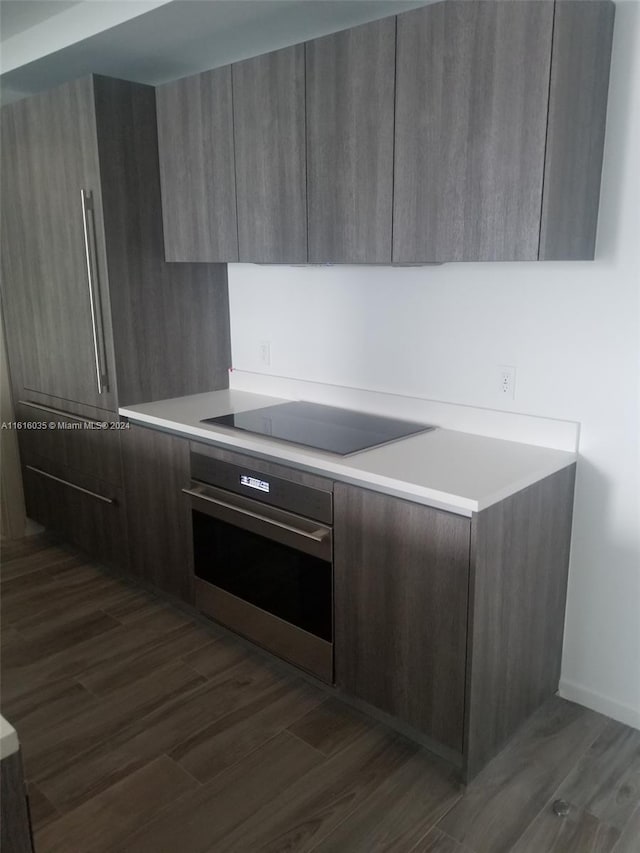 kitchen featuring dark wood-type flooring, black electric cooktop, and stainless steel oven