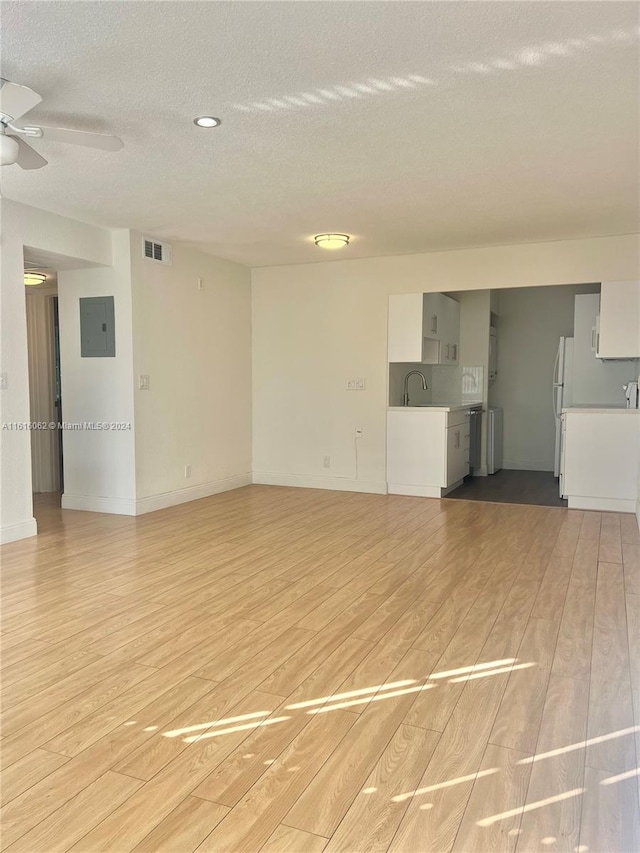 interior space featuring a textured ceiling, electric panel, light hardwood / wood-style flooring, and ceiling fan