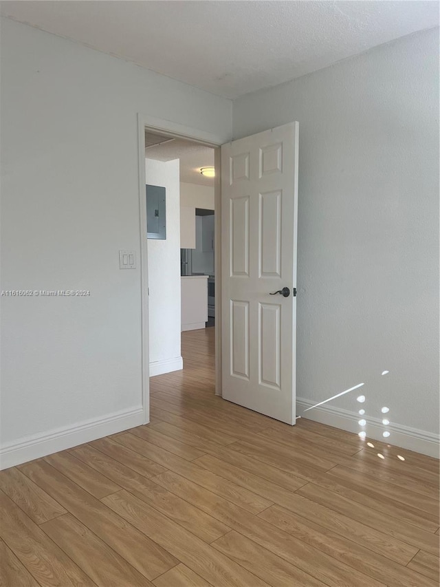 spare room with a textured ceiling, electric panel, and light hardwood / wood-style flooring