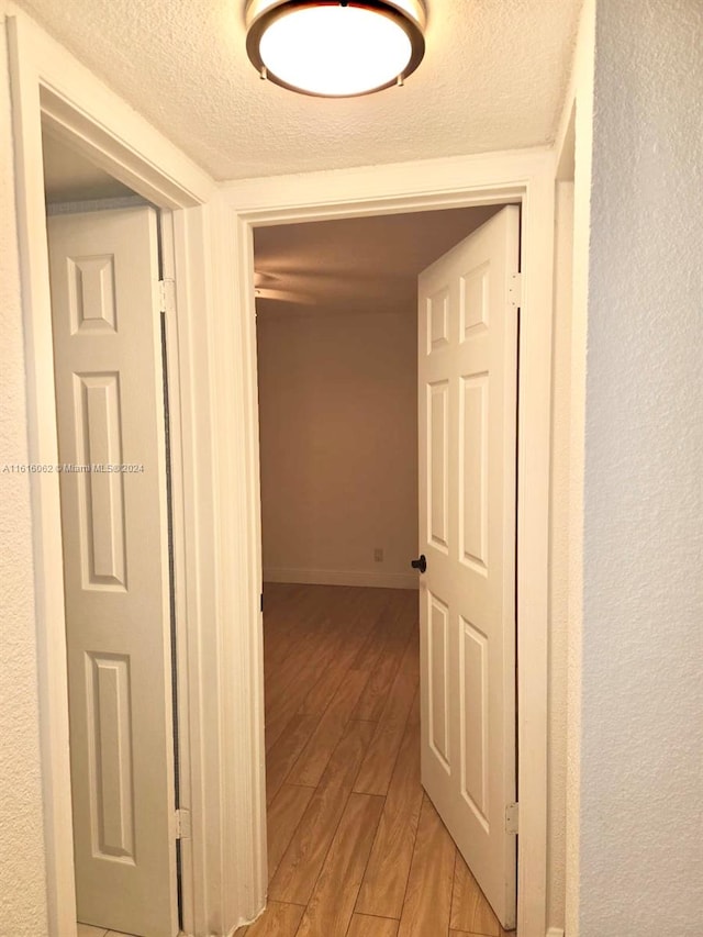 corridor with a textured ceiling and light wood-type flooring